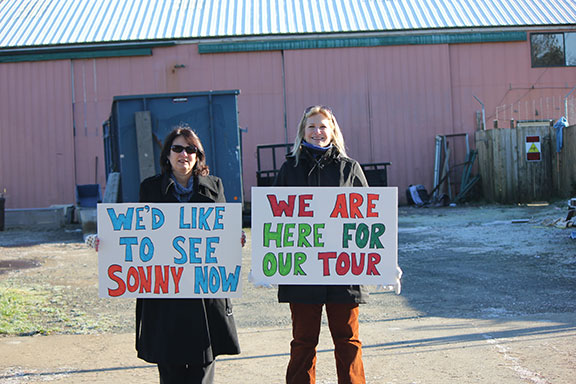 Tamira and Robin stand in front of the pink metal warehouse containing as many as 120 dogs with their signs requesting a tour and to see Sonny